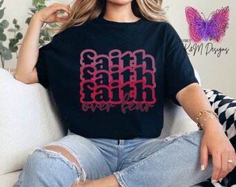 May include: Black t-shirt with the words "faith over fear" in a stacked, layered design with pink and red gradient coloring. The shirt is worn with blue jeans.