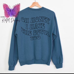 May include: A blue sweatshirt with the text "Oh honey I hate the devil too" printed on the back in a black, retro font.