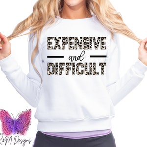 Peut inclure: Sweat-shirt blanc avec un motif léopard qui dit "EXPENSIF et DIFFICILE" en texte noir.