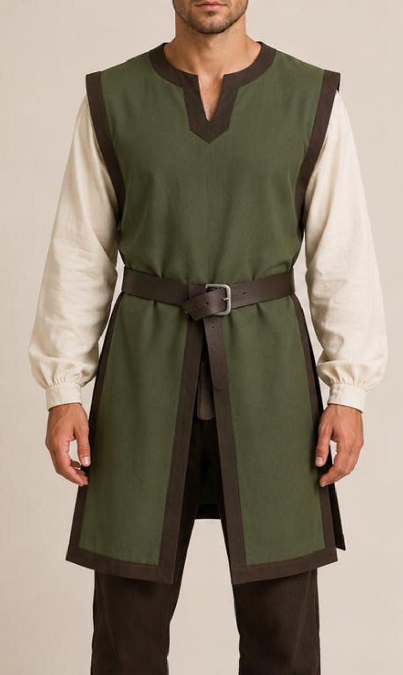 May include: A sleeveless olive green tunic featuring dark brown trim along the edges and a notched neckline. The tunic is worn over a long-sleeved cream-colored shirt and is cinched at the waist with a dark brown leather belt with a metal buckle.