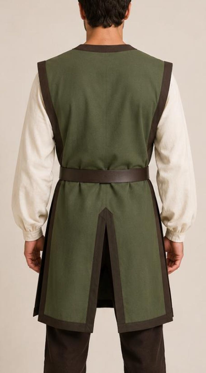 May include: A sleeveless olive green tunic with dark brown trim along the edges, worn over a long-sleeved cream-colored shirt. A dark brown belt is cinched at the waist. The tunic features a split back hem and is paired with dark brown trousers.