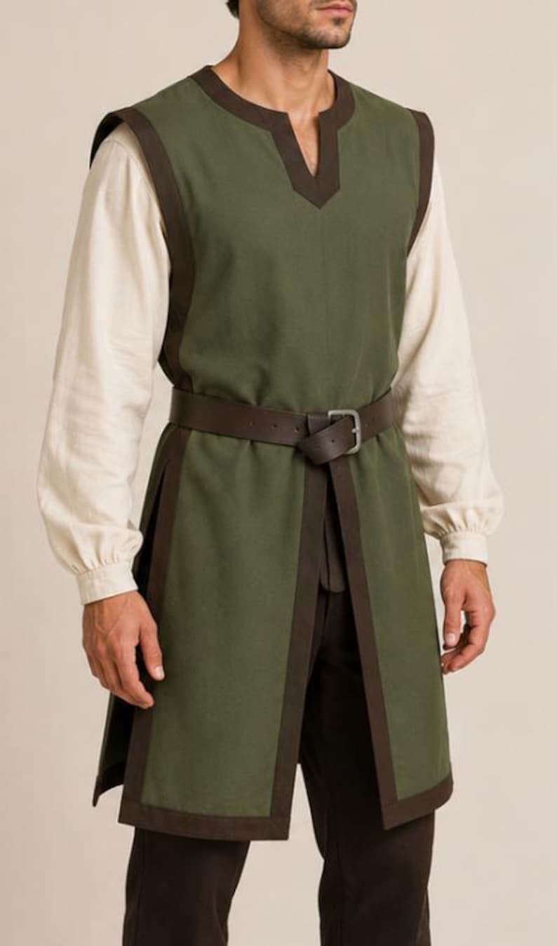 May include: An olive green sleeveless tunic featuring dark brown trim along the edges, a notched neckline, and side slits. The tunic is worn over a long-sleeved cream-colored shirt and dark brown trousers, cinched at the waist with a brown leather belt.