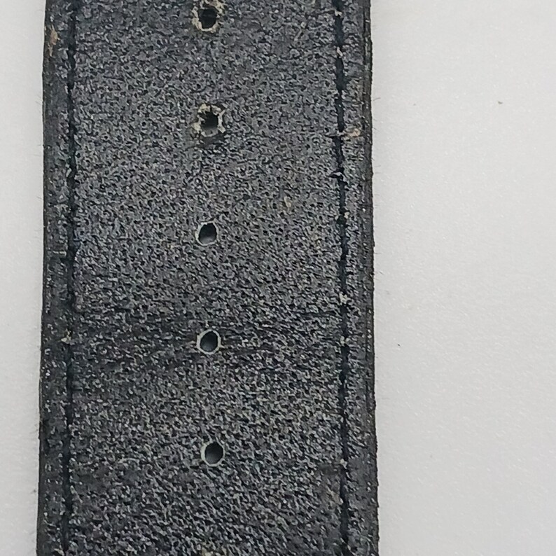 May include: A close-up of a black leather watch strap with four holes for adjusting the size.