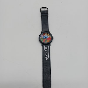 May include: A black wristwatch with a colorful, abstract design on the face. The watch has a black leather band and the artist's signature, "Licht", is printed on the band.