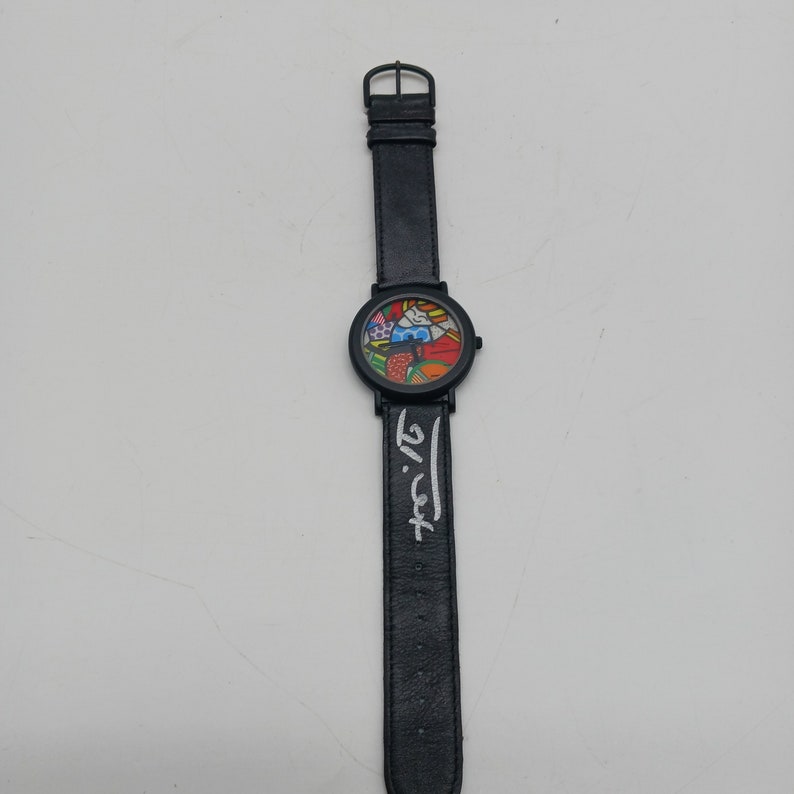 May include: A black wristwatch with a colorful, abstract design on the face. The watch has a black leather band and the artist's signature, "Licht", is printed on the band.