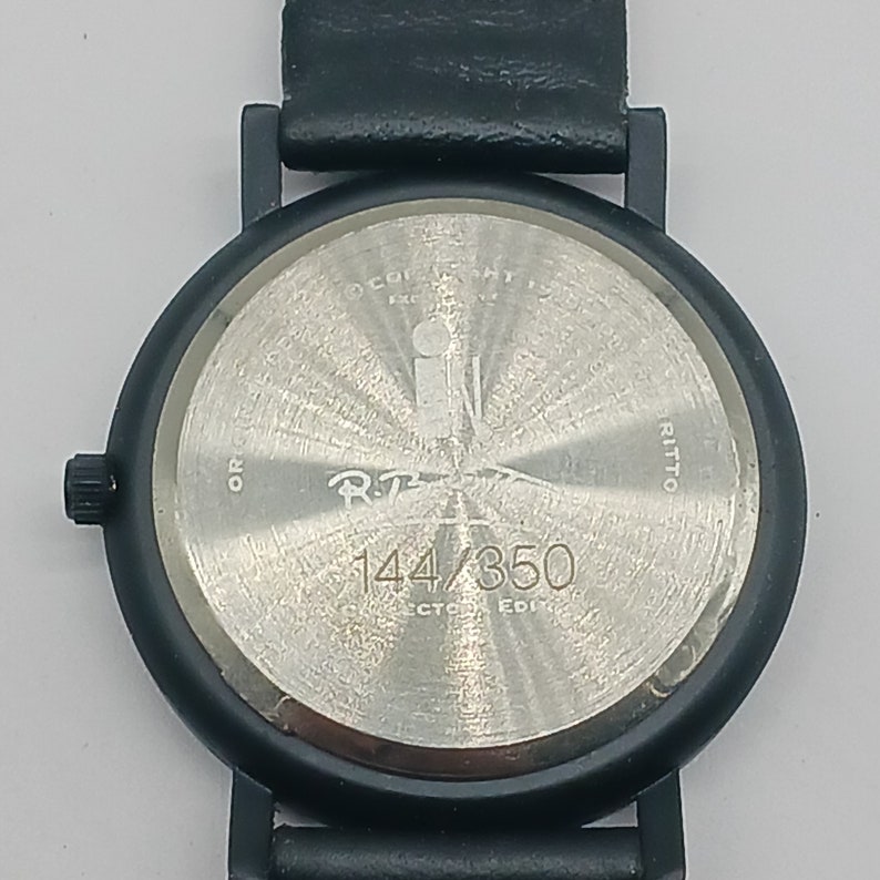 May include: Black wristwatch with a silver face and black leather band. The watch face has the text "R.T. 144/350" printed on it.