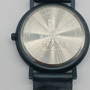 May include: Black wristwatch with a silver face and black leather band. The watch face has the text "R.T. 144/350 COLLECTORS EDITION" on it.