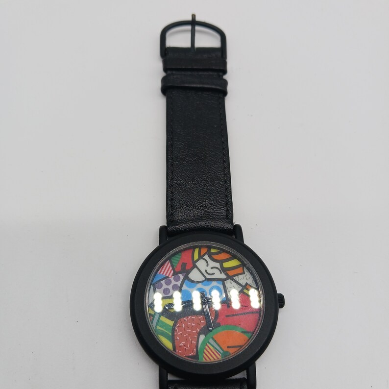 May include: Black leather wristwatch with a colorful abstract design on the face. The watch has a black leather band and a silver buckle.