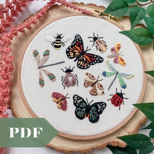 May include: A white embroidery hoop featuring a selection of colourful embroidered insects, including butterflies, dragonflies, moths and beetles. The hoop is displayed on a wooden surface.