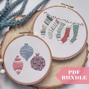 Pode incluir: Dois bastidores de bordado com desenhos natalinos. Um apresenta meias de Natal bordadas penduradas em uma corda. O outro tem três enfeites pendurados. Os bastidores estão sobre uma fatia de madeira com um elemento decorativo azul.