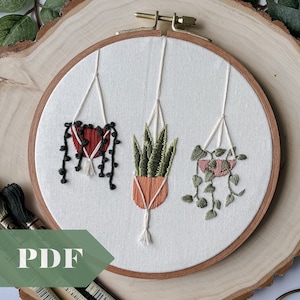 Op de afbeelding: Een borduurring met drie geborduurde hangplanten. De planten staan in terracotta potten en macramé hangers. De planten zijn een hartvormige plant, een vetplant en een hangplant. Het woord "PDF" staat linksonder.