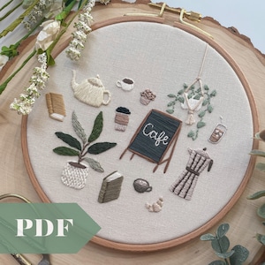 May include: Embroidered hoop art featuring a cosy cafe scene with a coffee pot, coffee cups, books, plants, and a chalkboard sign that says "Cafe".