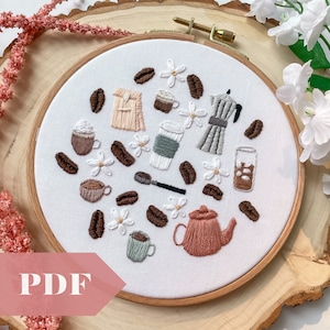 Könnte beinhalten: Stickerei in einem runden Rahmen mit Kaffeethema, mit braunen Kaffeebohnen, weißen Blumen und verschiedenen Kaffeeutensilien wie einer Kaffeekanne, Tassen und einer Tasse Kaffee.