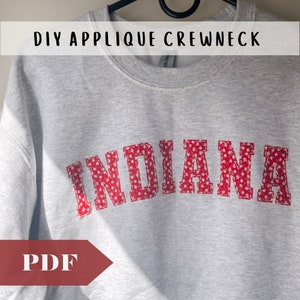 Może przedstawiać: Szara bluza z czerwoną aplikacją słowa "INDIANA" w białym wzorze kwiatowym. Bluza ma okrągły dekolt, a tekst "DIY APPLIQUE CREWNECK PDF" znajduje się w górnej części obrazu.