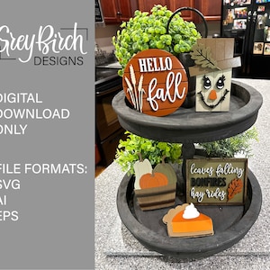 May include: A three-tiered wooden tray with fall-themed decorations. The top tier features a round wooden sign that says "Hello Fall" with wheat stalks and a scarecrow. The middle tier has a small wooden basket with pumpkins and gourds. The bottom tier has a wooden sign that says "Leaves Falling, Bonfires, Hay Rides" with a leaf and a pumpkin.