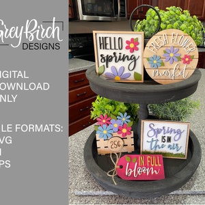 May include: A tiered tray arrangement featuring spring-themed wooden signs and floral accents. The signs include phrases like "Hello Spring" and "Fresh Flower Market." The arrangement also includes a wooden crate with flowers and a tag that says "In Full Bloom."