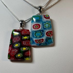 Op de afbeelding: Twee zilveren kettingen met rechthoekige glazen hangers. De hangers hebben een kleurrijk mozaïekpatroon met rode, blauwe, gele en witte bloemen.