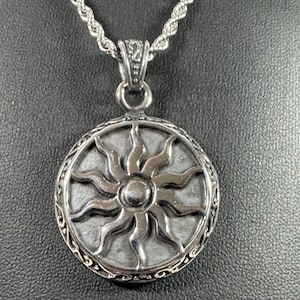 May include: Silver-toned pendant necklace featuring a detailed sunburst design within a circular frame. The pendant hangs from a matching twisted rope chain. The sun design has multiple rays extending from a central circle.