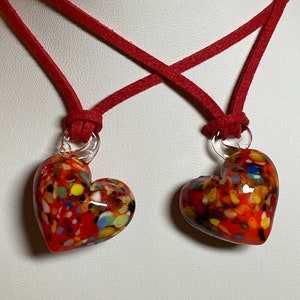 May include: A red suede cord necklace with two red, white and multi-coloured glass heart pendants.