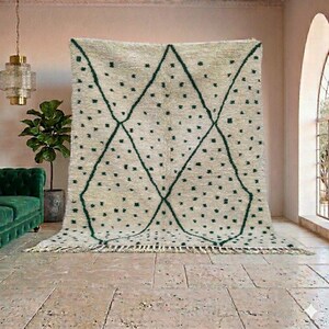 May include: A large, cream-colored rug with a geometric design. The rug features a diamond pattern in dark green, with small green dots scattered across the surface. The rug has a fringe along the bottom edge.