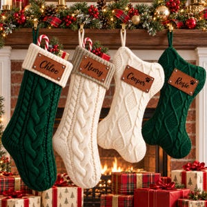 Puede incluir: Cuatro calcetines navideños de punto trenzado en colores verde oscuro y crema, cada uno con un parche de cuero marrón personalizado con los nombres Chloe, Henry, Cooper y Rosie, colgados de una repisa decorada con vegetación y luces.