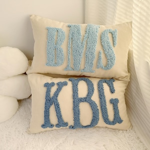 Könnte beinhalten: Zwei weiße Kissen mit blauen Stickbuchstaben. Das obere Kissen hat die Buchstaben "BMS" und das untere Kissen die Buchstaben "KBG".