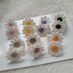 Op de afbeelding: Een set van 10 witte daisy haar elastiekjes met verschillende gekleurde centra. De centra zijn roze, geel, paars, bruin, zwart en oranje.