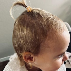 以下が含まれることがあります： 黄色い花のヘアゴムでポニーテールに結ばれた金髪の小さな子供