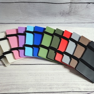 May include: A set of 11 colorful wallets with elastic bands. The wallets are arranged in a fan shape, with the black wallet at the bottom.