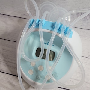 K&ouml;nnte beinhalten: Eine blaue und wei&szlig;e elektrische Milchpumpe mit digitalem Display und klaren Schl&auml;uchen. Die Pumpe hat einen Zyklusknopf, einen Ein- und Ausschalter und einen Knopf zum Einstellen des Sauggrads.