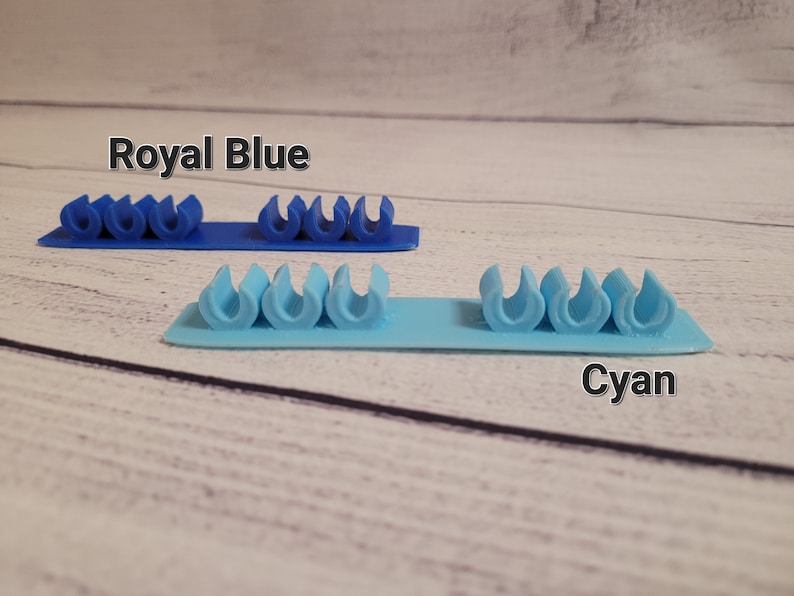 K&ouml;nnte beinhalten: Zwei Reihen Kabelorganizer, eine in Royalblau und eine in Cyan. Jede Reihe hat f&uuml;nf Kabelorganizer.