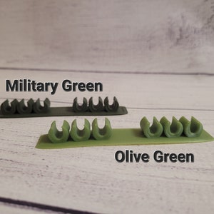 K&ouml;nnte beinhalten: Zwei Reihen Kabelorganizer in Milit&auml;rgr&uuml;n und Olivgr&uuml;n. Die Organizer sind aus Kunststoff und haben eine Reihe kleiner Schlaufen zum Halten von Kabeln.
