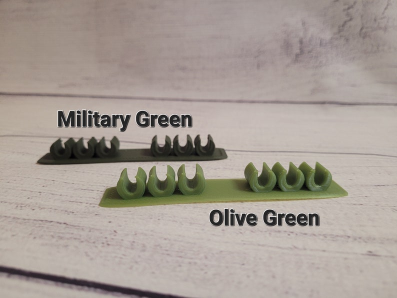 K&ouml;nnte beinhalten: Zwei Reihen Kabelorganizer in Milit&auml;rgr&uuml;n und Olivgr&uuml;n. Die Organizer sind aus Kunststoff und haben eine Reihe kleiner Schlaufen zum Halten von Kabeln.