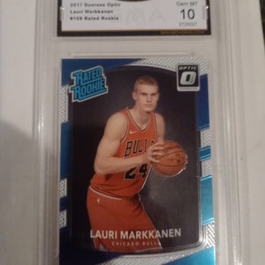 May include: A blue and white basketball card featuring Lauri Markkanen, a basketball player for the Chicago Bulls. The card is graded Gem Mint 10 by GMA Grading. The card is from the 2017 Donruss Optic series.