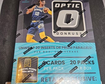 May include: A box of 2021-22 Panini Optic NBA basketball trading cards featuring Ja Morant of the Memphis Grizzlies. The box is black with a silver and white Optic logo and the text "Donruss" printed on it. The box includes 20 packs of cards, with 4 cards per pack. The box also includes 20 inserts or Prizm parallels.