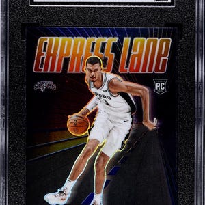 Puede incluir: Una tarjeta de baloncesto 2023-24 Donruss Optic Victor Wembanyama Express Lane Purple Prizm calificada con 9.5 por SGC. La tarjeta muestra al jugador con un uniforme blanco de los San Antonio Spurs driblando un bal&oacute;n sobre un fondo morado y negro.