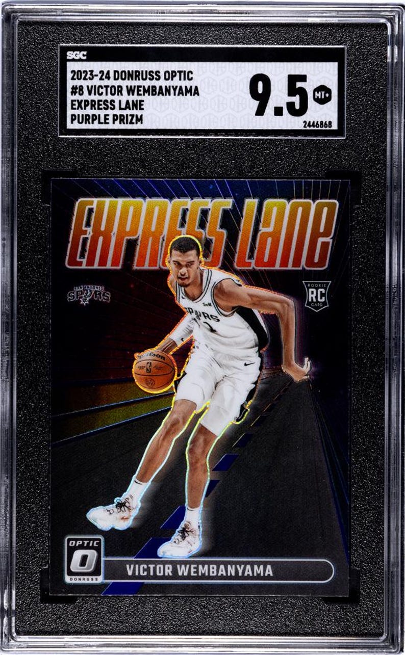 Puede incluir: Una tarjeta de baloncesto 2023-24 Donruss Optic Victor Wembanyama Express Lane Purple Prizm calificada con 9.5 por SGC. La tarjeta muestra al jugador con un uniforme blanco de los San Antonio Spurs driblando un bal&oacute;n sobre un fondo morado y negro.