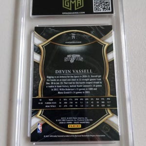 Puede incluir: Una tarjeta de intercambio con Devin Vassell, un jugador de baloncesto de los San Antonio Spurs. La tarjeta es dorada y negra con una foto de Vassell con su uniforme. El n&uacute;mero de la tarjeta es 71. La tarjeta incluye estad&iacute;sticas de la carrera de Vassell.