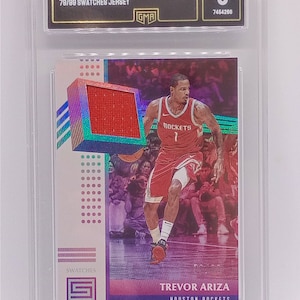 May include: A graded trading card featuring Trevor Ariza of the Houston Rockets. The card includes a red jersey swatch and the text "2017 STATUS TREVOR ARIZA 79/99 SWATCHES JERSEY". The card is graded NM-MT 8 by GMA.