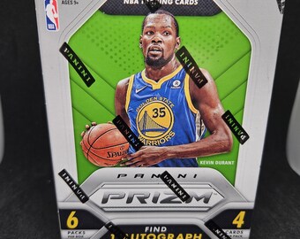 Puede incluir: Una caja de cartas de intercambio de la NBA Panini Prizm 2018-19 con Kevin Durant de los Golden State Warriors. La caja tiene un fondo verde con una imagen de Durant driblando un balón de baloncesto. La caja dice "¡Encuentra 1 autógrafo o memorabilia! Por caja, en promedio".