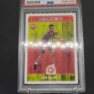 以下が含まれることがあります： 2017年パニーニフープス、ジョン・コリンズのバスケットボールカード。GEM MT 10と評価され、保護ホルダーに入っています。カードには、NBAフープスのロゴと「RC」ルーキーカードの文字とともに、ジョン・コリンズのプレー写真が写っています。ホルダーは透明です。
