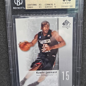 Puede incluir: Una tarjeta de intercambio de baloncesto con Kawhi Leonard, un jugador de baloncesto de San Diego State. La tarjeta está calificada con un 9.5 por Beckett Grading Services y tiene una condición Gem Mint. La tarjeta es de la serie SP Authentic 2011-12.