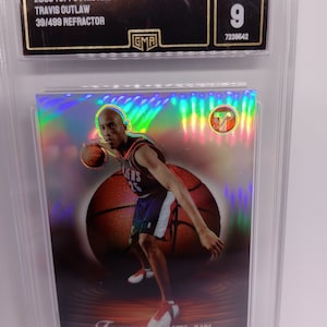 May include: A basketball trading card featuring Travis Outlaw of the Portland Trail Blazers. The card is graded MINT 9 by GMA. The card is a 2003 Topps Pristine Refractor, numbered 39/499. The card shows Outlaw in action, dribbling a basketball.