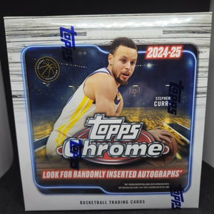 Puede incluir: Una caja de cartas coleccionables de baloncesto Topps Chrome con Stephen Curry. La caja tiene un diseño azul y plateado con el texto "2024-25" y "Busca autógrafos insertados aleatoriamente."