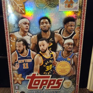 Peut inclure: Un calendrier de l'Avent Topps Holiday avec des joueurs de basket-ball. La boîte présente un design festif avec des bonhommes en pain d'épices et un timbre avec une maison. Le calendrier comprend 24 paquets de vacances et des parallèles exclusifs à carreaux. L'année est 2025/26.