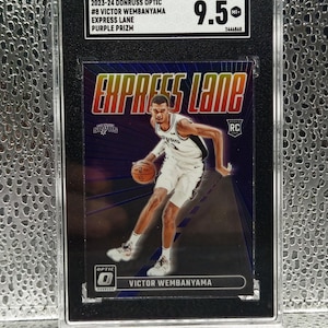 Puede incluir: Una tarjeta de baloncesto 2023-24 Donruss Optic Victor Wembanyama Express Lane Purple Prizm calificada con 9.5 por SGC. La tarjeta muestra al jugador con el uniforme de los San Antonio Spurs driblando un bal&oacute;n sobre un fondo morado con el texto Express Lane.