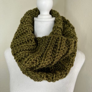 May include: A green crocheted infinity scarf on a white mannequin.