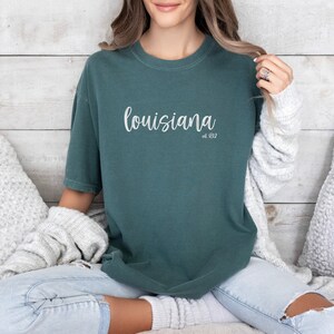 May include: A teal blue t-shirt with the text "louisiana est. 1812" in white lettering.