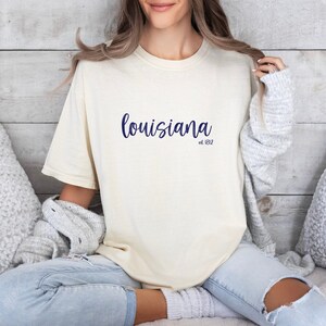 May include: A white t-shirt with the text "louisiana est. 1812" printed in blue.