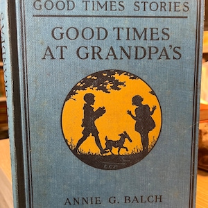 Puede incluir: Un libro azul con el título "Good Times Stories Good Times At Grandpa's" de Annie G. Balch. La portada presenta una ilustración de silueta de dos niños y un perro en un círculo amarillo.
